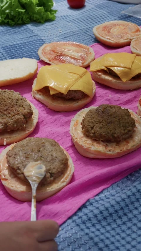 Assembling Multiple Cheeseburgers on Pink Mat During Picnic Prep Stock Footage 342001096