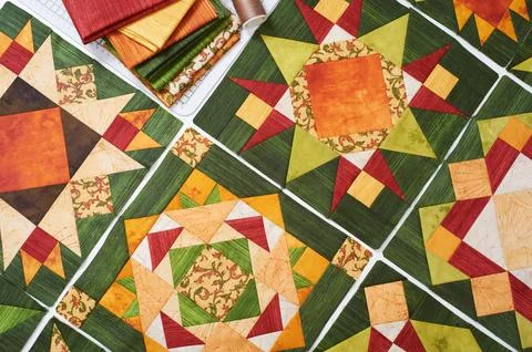 Assembling of quilt from orange-green patchwork blocks, pile of fabric Stock-Fotos
