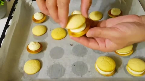 Assembling sweet sandwich cookies with white cream filling on baking sheet Stock Footage 327259107
