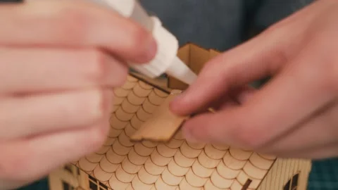 Assembling wooden house model with hands refining chimney structure during DIY Stock Footage 340195712