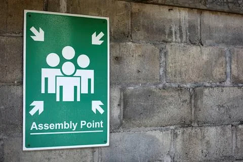 Assembly point sign on wall with group icon and arrows Stock Photos