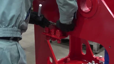 Assembly worker tightening large bolts with a wrench on a freshly painted red Stock Footage 341595075
