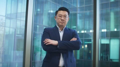 Assertive Asian male in glasses standing tall with folded arms in front of 스톡 동영상 317543444