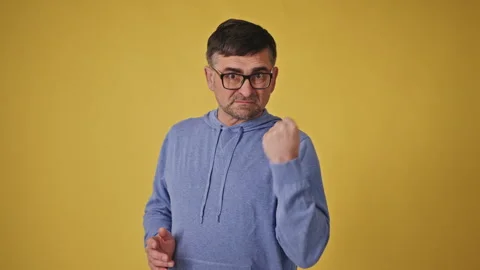 Assertive senior man in glasses making threatening gesture against yellow 스톡 동영상 265659310