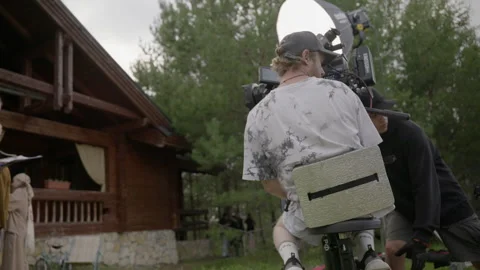 Assistant carefully pushes camera dolly along rails while keeping operator Stock Footage 303060173