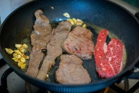 Assorted Beef Cuts and Garlic Sizzling in a Black Frying Pan on a Kitchen S.. Stock Photos