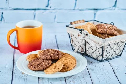 Assorted biscuits in plate and basket and a cup on blue table Stock Photos