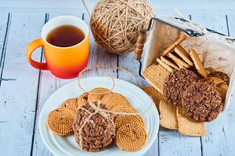 Assorted biscuits in plate and basket and a cup on blue table Stock Photos