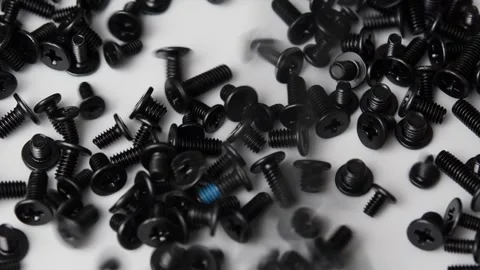 Assorted black screws fall across a white surface for electronics, computer Stock Footage 346875726