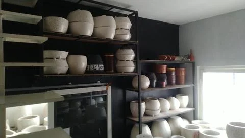 Assorted ceramic pots are displayed on a dark shelving unit Stock Photos