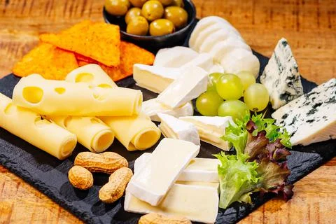 Assorted cheese on a black ceramic kitchen board with grapes, olives and nuts Stock Photos