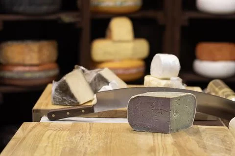 Assorted cheese blocks and knife on wooden board in a rustic cheese shop display Stock Photos