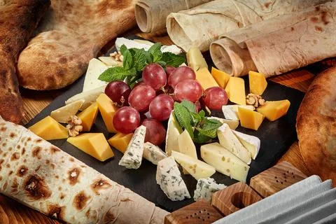 Assorted cheese board with grapes, walnuts and fresh mint on black slate, a.. Foto stock