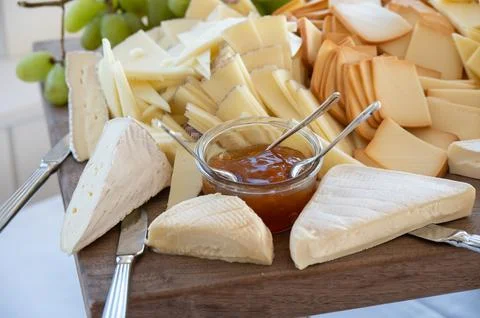 Assorted cheeses and jam served on wooden board with cheese kniv Stock Photos