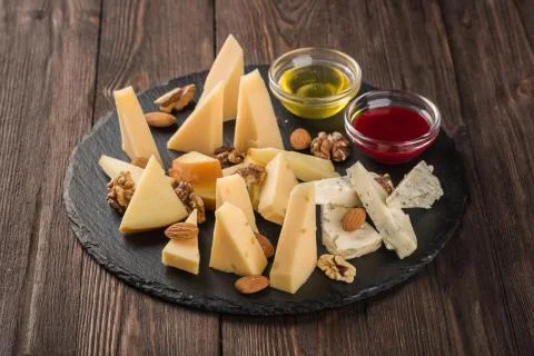 Assorted cheeses on a black dish. Served with nuts sauce and honey. Stock Photos