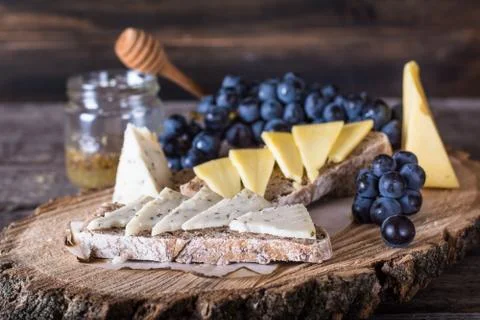 Assorted cheeses with grapes, bread, honey on dark wood background. Goat chee Stock Photos