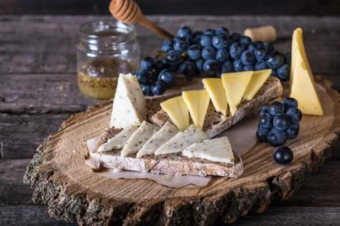 Assorted cheeses with grapes, bread, honey on dark wood background. Goat chee Stock Photos