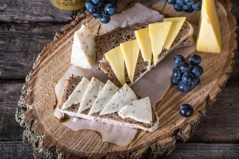 Assorted cheeses with grapes, bread, honey on dark wood background. Goat chee Stock Photos