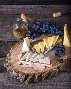 Assorted cheeses with grapes, bread, honey on dark wood background. Goat chee Stock Photos