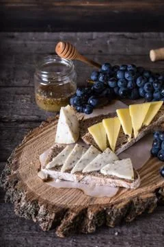 Assorted cheeses with grapes, bread, honey on dark wood background. Goat chee Stock Photos