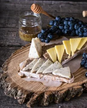 Assorted cheeses with grapes, bread, honey on dark wood background. Goat chee Stock Photos