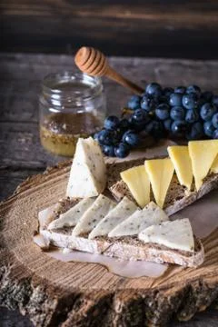 Assorted cheeses with grapes, bread, honey on dark wood background. Goat chee Stock Photos