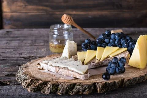 Assorted cheeses with grapes, bread, honey on dark wood background. Goat chee Stock Photos