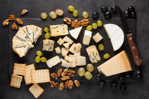 Assorted cheeses with white grapes, walnuts, crackers and white wine on a sto Stock Photos