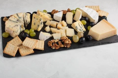Assorted cheeses with white grapes, walnuts, crackers and on a stone Board. F Stock Photos