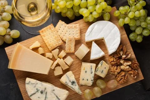 Assorted cheeses with white grapes, walnuts, crackers and white wine on a woo Stock Photos