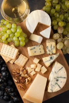 Assorted cheeses with white grapes, walnuts, crackers and white wine on a woo Stock Photos