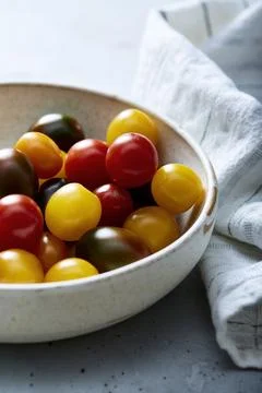 Assorted cherry tomatoes in ceramic bowl on blue surface Stock Photos
