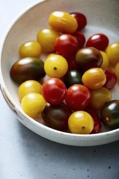 Assorted cherry tomatoes in ceramic bowl on blue surface Stock Photos