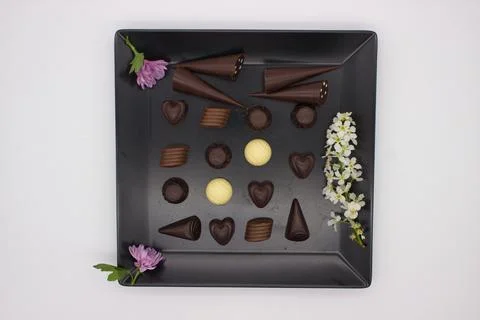 Assorted Chocolates with Blossoms and Purple Flower on Black Plate Stock Photos