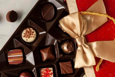 Assorted chocolates in elegant red gift pack with golden ribbon put on top Stock Photos