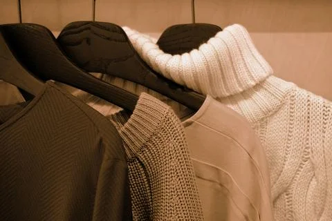 Assorted cozy sweaters hanging in a warm-toned wardrobe display Stock Photos