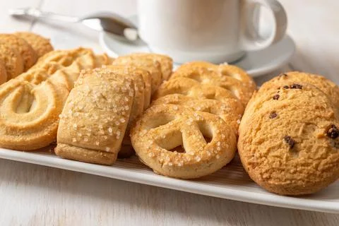 Assorted crispy shortbread biscuits on a rectangular plate and white tea cup. Stock Photos