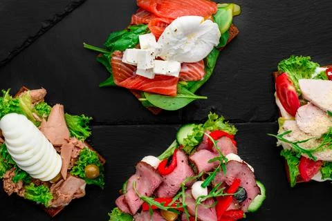 Assorted different toasts with salmon, meat, eggs, tomatoes and cheese on black Stock Photos