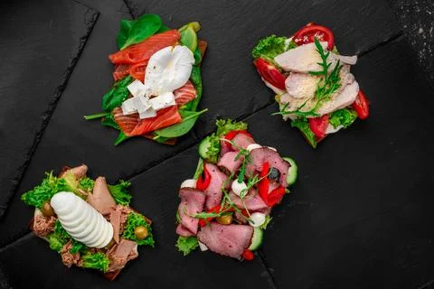 Assorted different toasts with salmon, meat, eggs, tomatoes and cheese on black Stock Photos