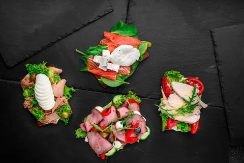 Assorted different toasts with salmon, meat, eggs, tomatoes and cheese on black Stock Photos