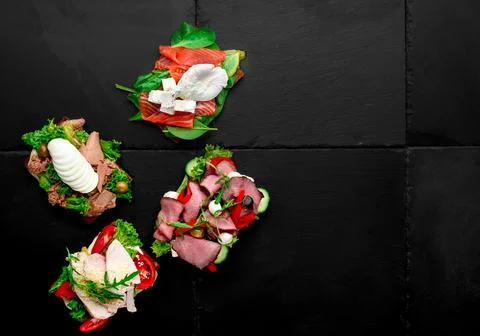 Assorted different toasts with salmon, meat, eggs, tomatoes and cheese on black Stock Photos