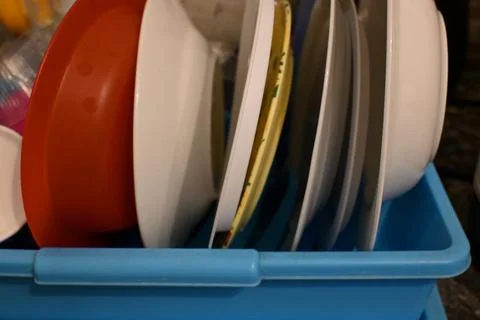 Assorted dinner plates stand upright in a blue plastic dish rack. Close-up co 库存照片