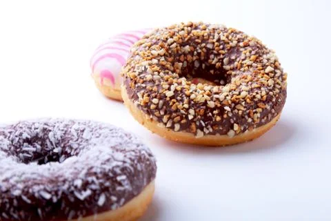 Assorted doughnuts in the glaze, colorful sprinkles and nuts on a white Stock Photos