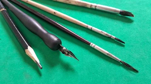 Assorted drawing pencils and professional paint brushes on green surface Stock Photos