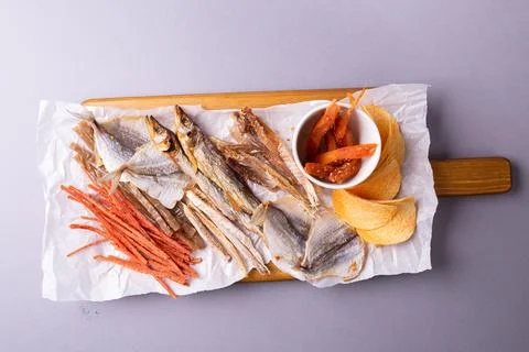 Assorted dried fish, fish skin, and fruit snacks on white paper on a wooden t Stock Photos