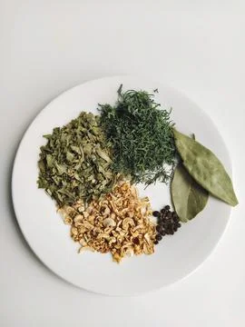 Assorted dried herbs on white plate: parsley, dill, celery, bay leaf and blac Stock Photos