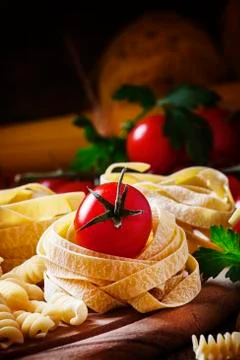 Assorted dry pasta, cherry tomatoes and parsley on a vintage wooden backgroun Stock Photos
