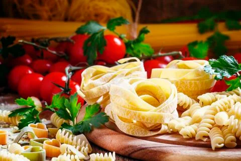 Assorted dry pasta, cherry tomatoes and parsley on a vintage wooden backgroun Stock Photos