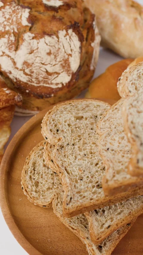 Assorted Fresh Bakery Bread and Sliced Whole Wheat Toast on Wooden Plate Stock Footage 337917708