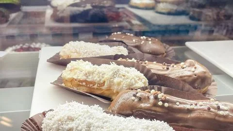 Assorted fresh eclairs with chocolate glaze and white coconut topping on di.. Stock Photos